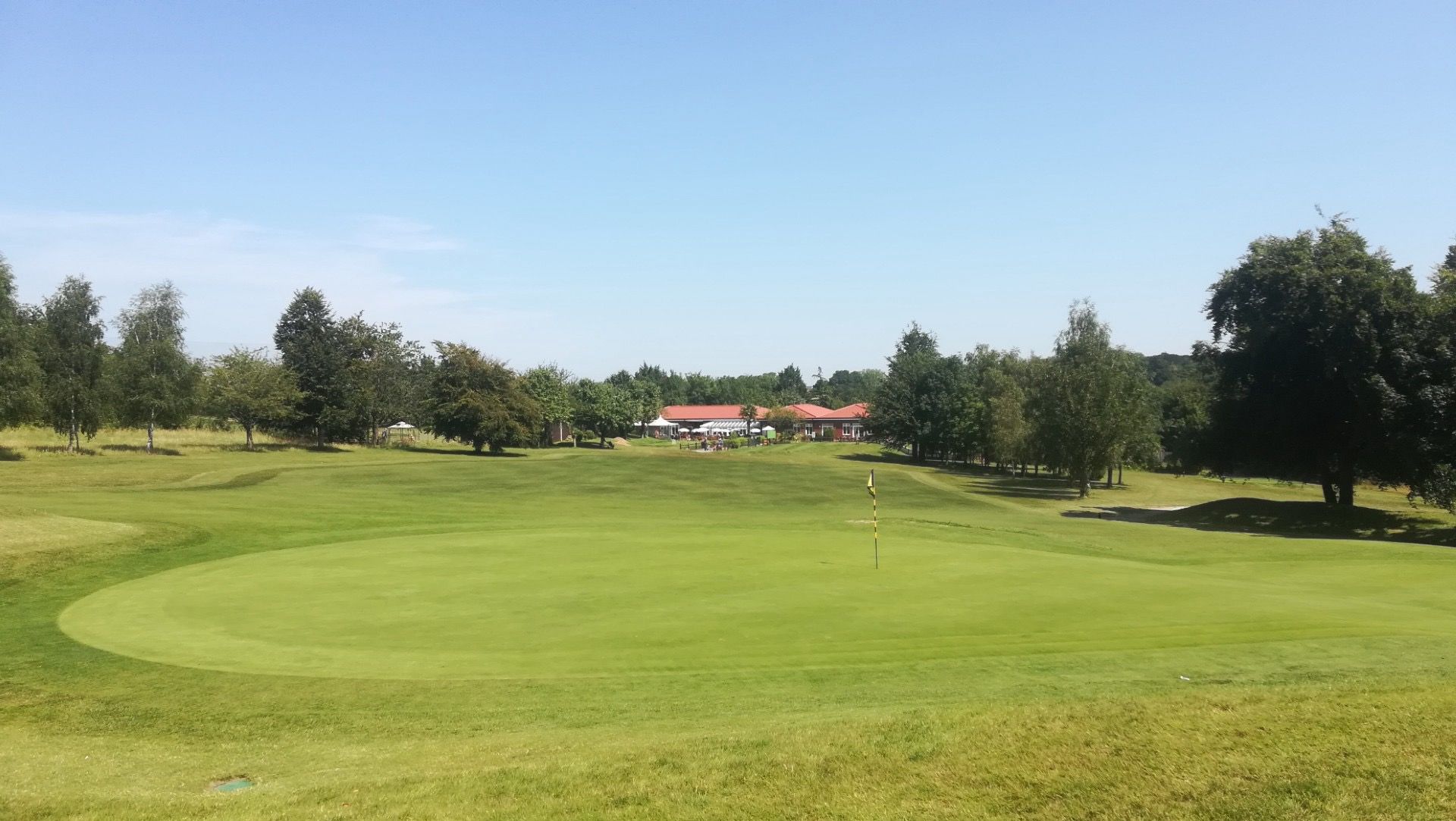 The yellow flag on the green with The Oaks clubhouse in the distance, Carshalton, Surrey